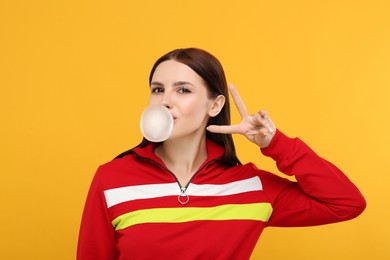 Photo of Beautiful woman blowing bubble gum and gesturing on orange background