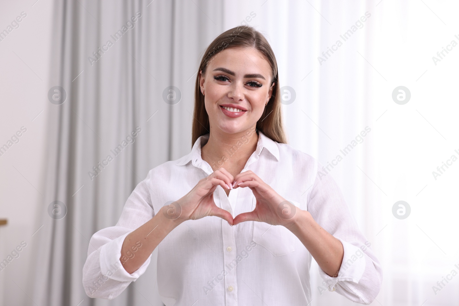 Photo of Happy woman showing heart gesture with hands indoors