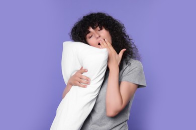 Photo of Tired young woman with pillow yawning on purple background. Insomnia problem