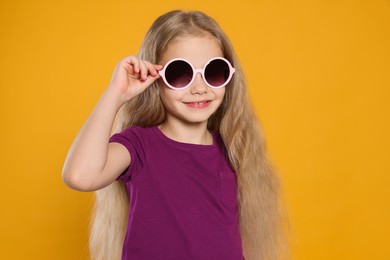 Girl in stylish sunglasses on orange background