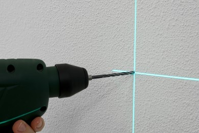 Photo of Using cross line laser level for accurate measurement and drilling hole in white wall, closeup