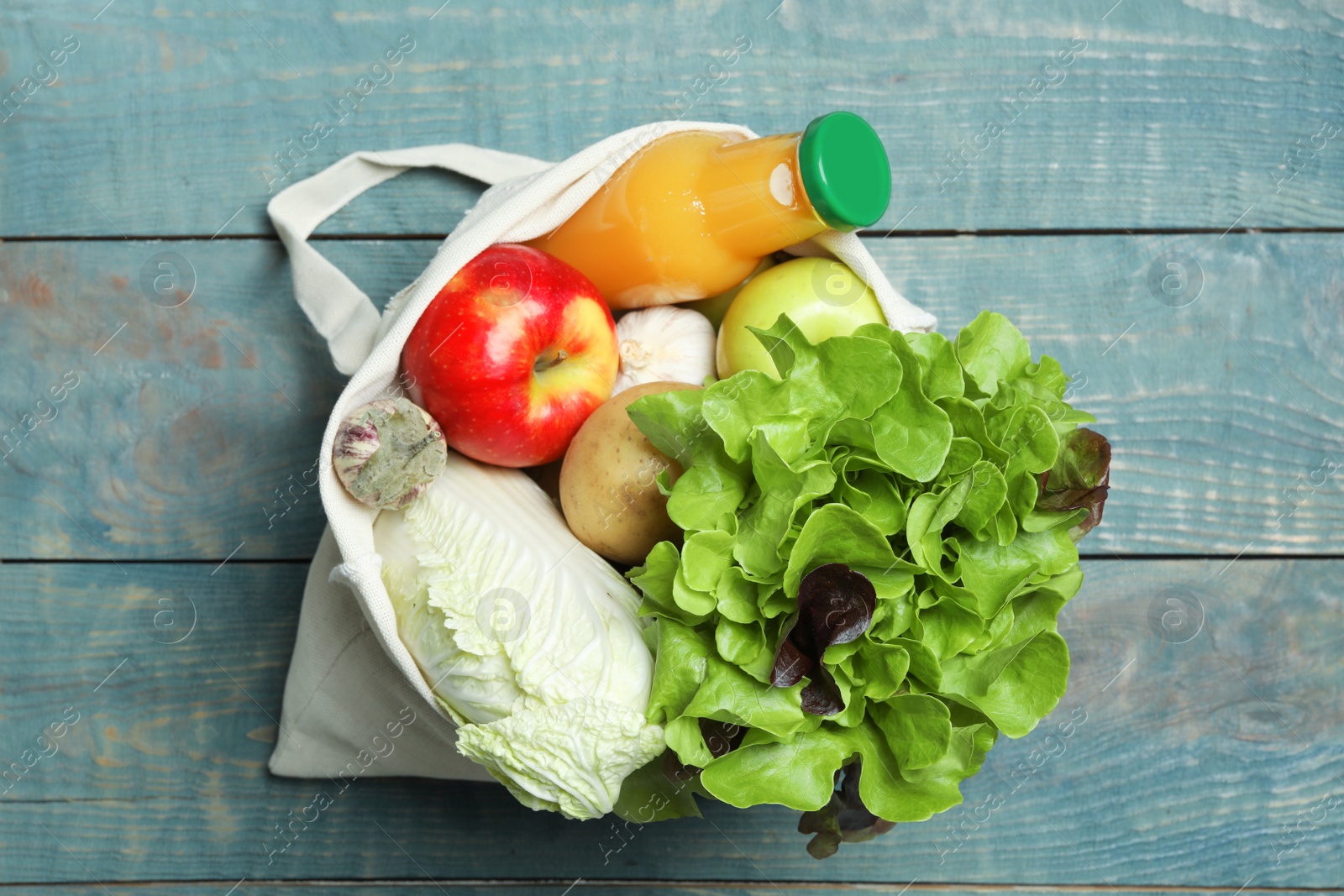 Photo of Bag with fresh vegetables, apples and bottle of juice on wooden background, top view
