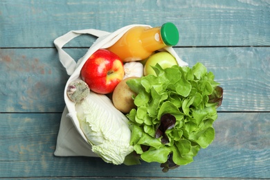 Photo of Bag with fresh vegetables, apples and bottle of juice on wooden background, top view