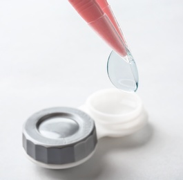 Photo of Tweezers with contact lens and container on light background, closeup