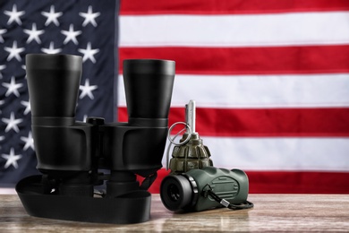 Photo of Military monocular, binocular and grenade on table against American flag background