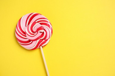 Photo of Stick with colorful lollipop swirl on yellow background, top view. Space for text