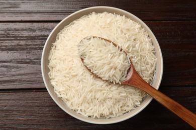 Photo of Raw basmati rice and spoon in bowl on wooden table, top view