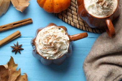 Flat lay composition with mugs of pumpkin spice latte on light blue wooden table