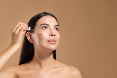 Photo of Beautiful young woman applying serum onto her face on beige background. Space for text