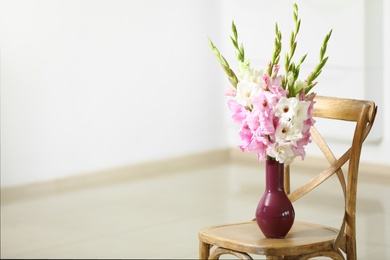 Vase with beautiful gladiolus flowers on wooden chair indoors. Space for text