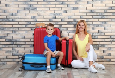 Photo of Woman and her son with suitcases near brick wall. Vacation travel
