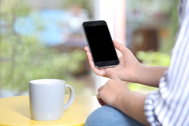 Woman holding smartphone with blank screen on blurred background. Mockup for design