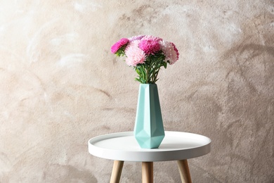 Beautiful aster flower bouquet in vase on table against color background