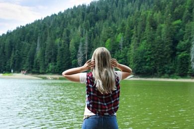 Woman near clear lake in green forest at summer, back view