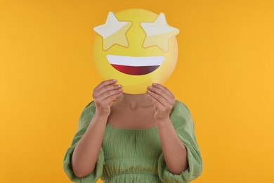 Woman holding emoticon with stars instead of eyes on yellow background