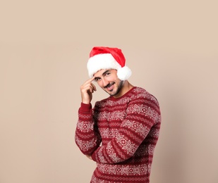 Portrait of young man in Christmas sweater and Santa hat on beige background