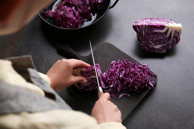 Woman cutting fresh red cabbage at black table, closeup