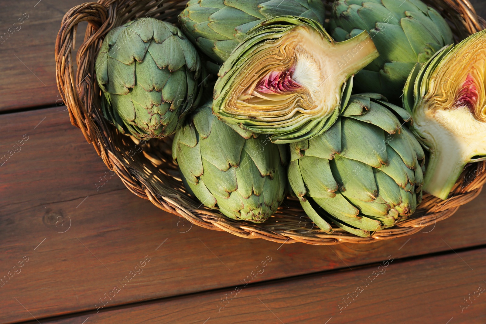 Photo of Wicker basket with fresh raw artichokes on wooden table, top view