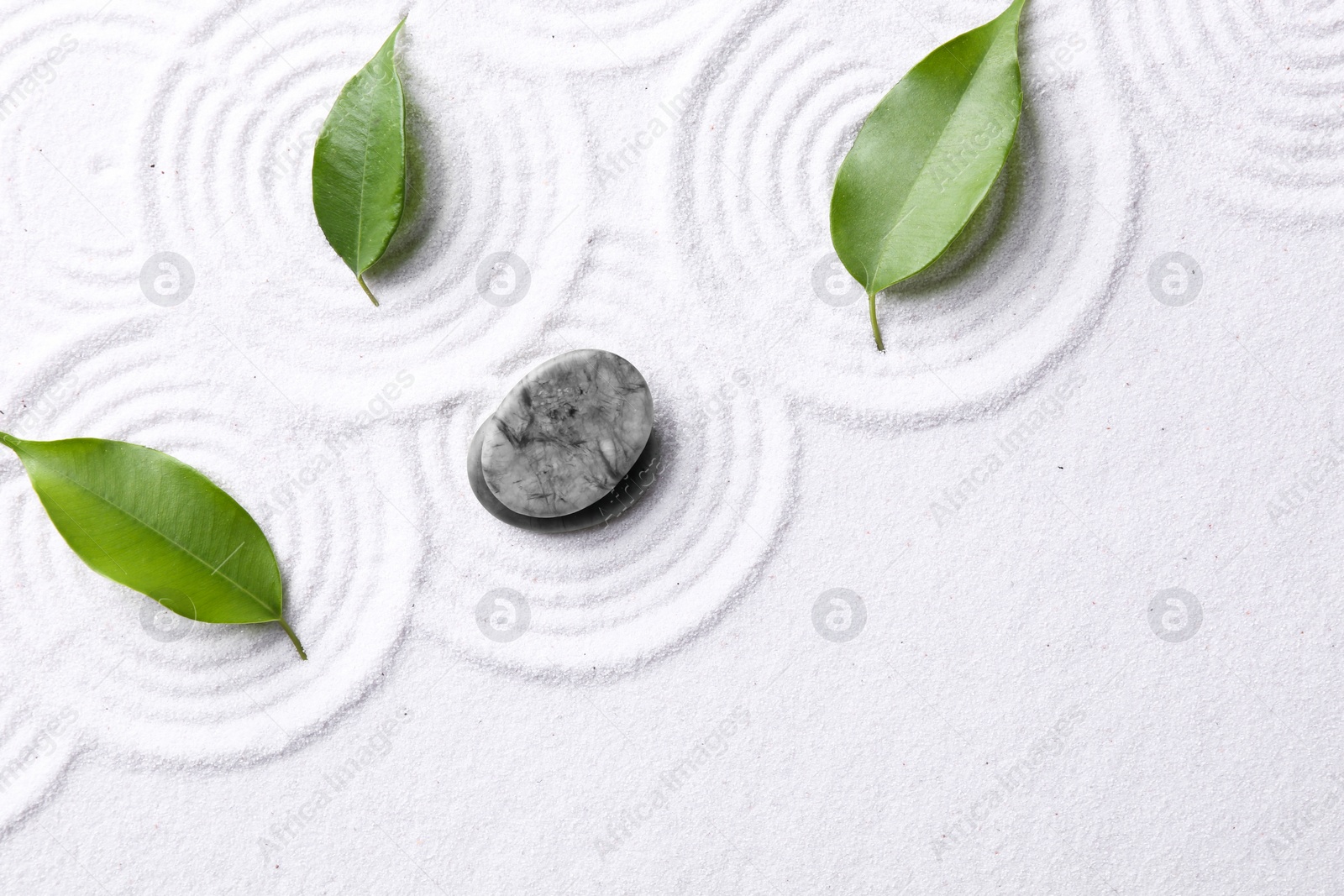 Photo of Zen garden stones and green leaves on white sand with pattern, flat lay. Space for text