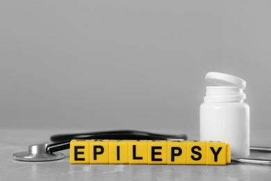 Photo of Blocks with word Epilepsy, stethoscope and bottle of pills on grey marble table, space for text