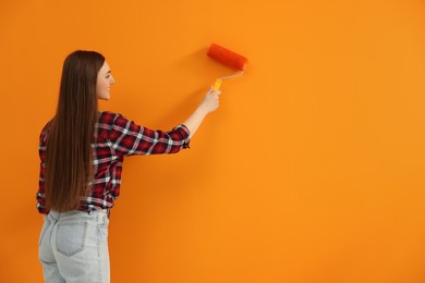Photo of Designer painting orange wall with roller, space for text