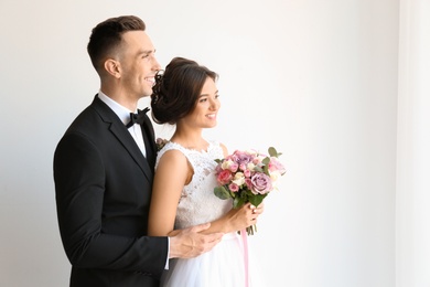 Young handsome groom and beautiful bride with bouquet on light background