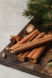 Board with different aromatic spices and fir branches on light table, closeup