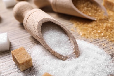 Scoops with different types of sugar on wooden table, closeup