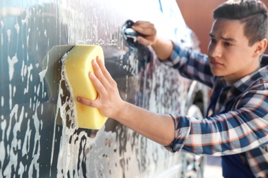 Photo of Worker cleaning automobile with sponge at car wash