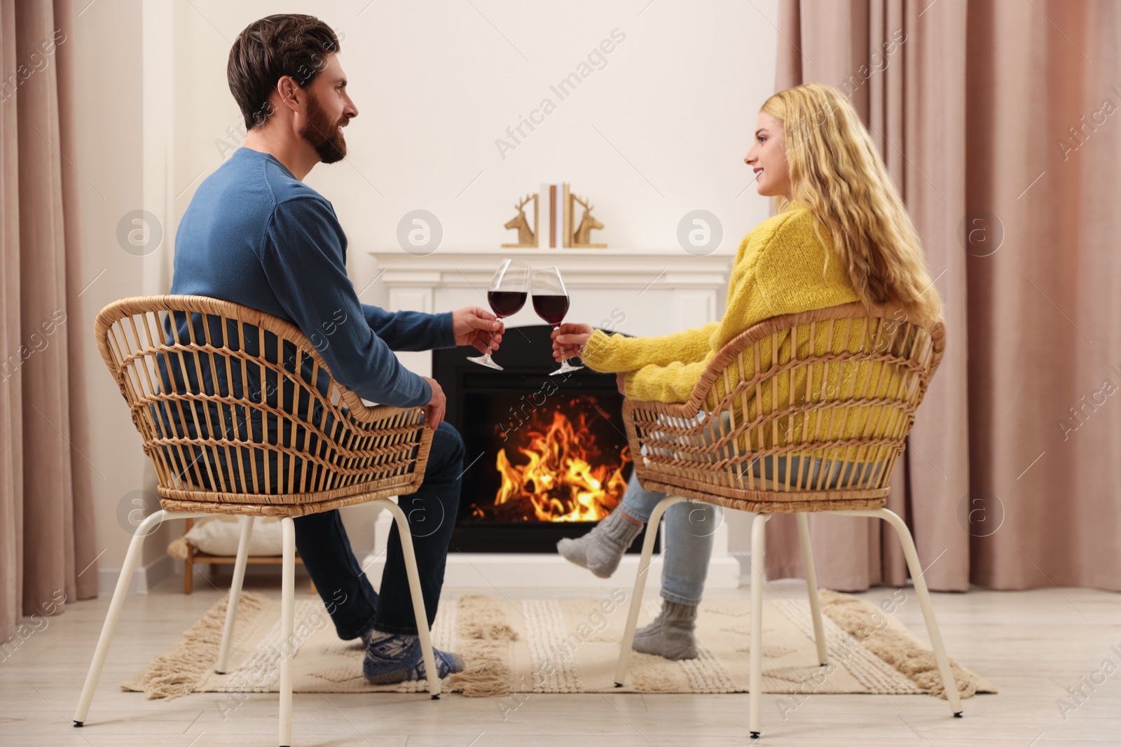 Photo of Lovely couple with glasses of wine spending time together near fireplace at home