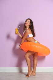 Photo of Beautiful young woman with inflatable ring and glass of cocktail near color wall