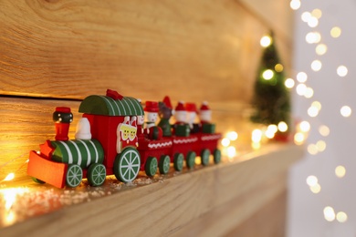 Photo of Bright toy train and Christmas lights on wooden shelf, closeup. Space for text