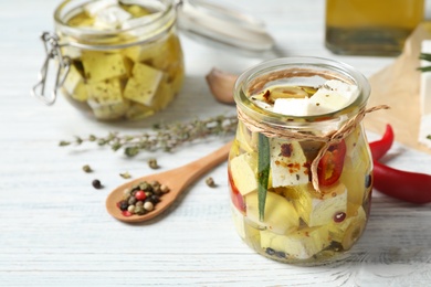 Jar with feta cheese marinated in oil on white wooden table. Pickled food