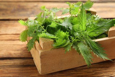 Photo of Fresh stinging nettle leaves in crate on wooden table, closeup