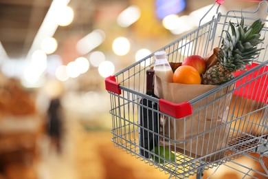 Image of Shopping cart with different groceries in supermarket, space for text