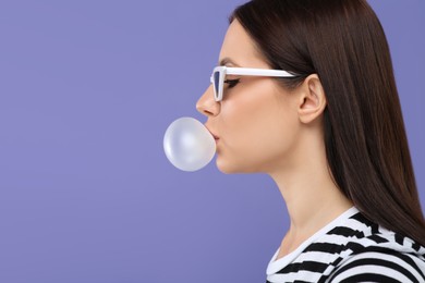 Photo of Beautiful woman in sunglasses blowing bubble gum on light purple background, space for text