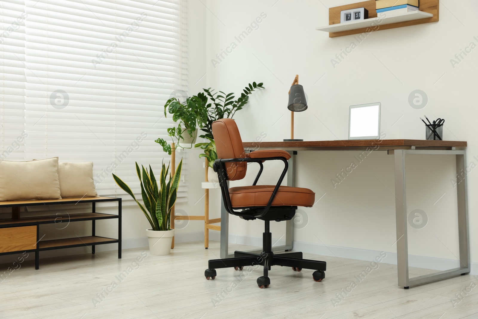 Photo of Stylish office interior with comfortable chair, desk, laptop and houseplants