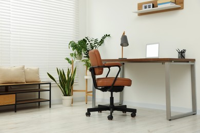 Stylish office interior with comfortable chair, desk, laptop and houseplants