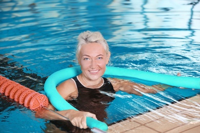 Photo of Sportive senior woman with swimming noodle in indoor pool