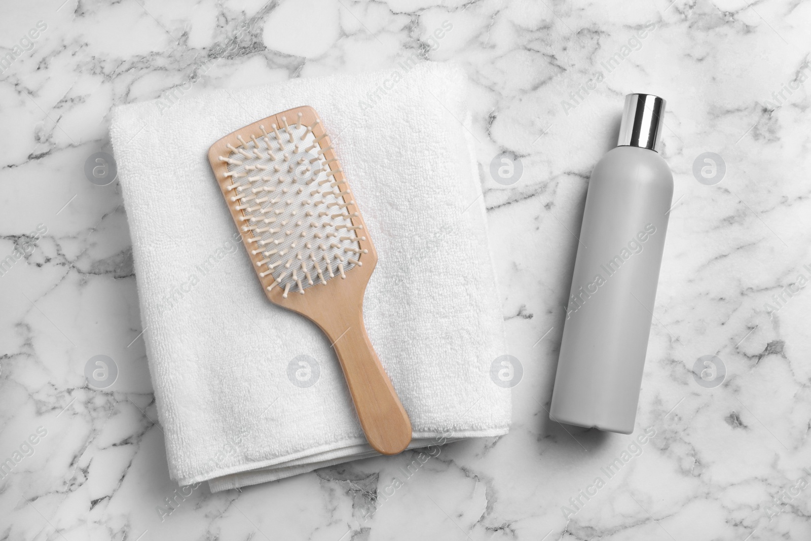 Photo of Towel, hair brush and shampoo on marble background, top view