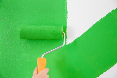 Photo of Woman painting white wall with green dye, closeup. Interior renovation