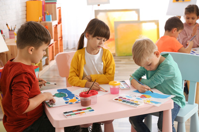 Photo of Cute little children painting at table in room