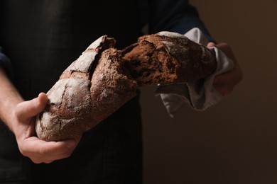 Photo of Man breaking loaf of fresh bread on dark background, closeup