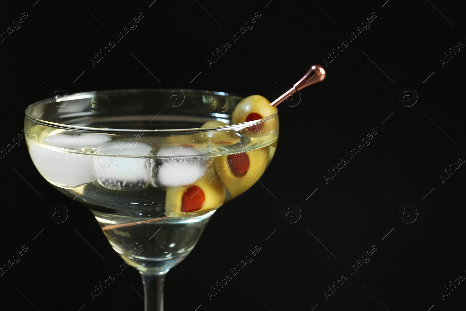 Photo of Martini cocktail with ice and olives on dark background, closeup. Space for text