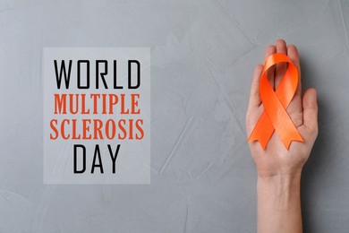 Multiple Sclerosis Awareness Day. Woman holding orange ribbon on light grey background, top view