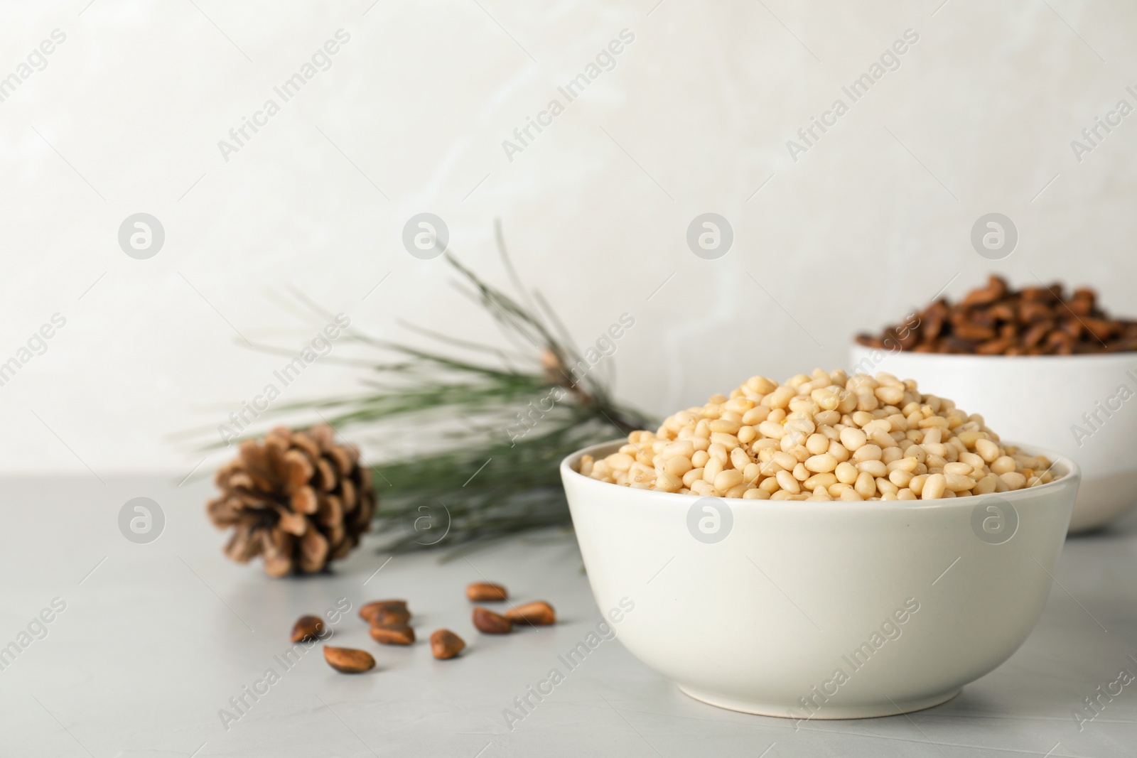 Photo of Bowl with pine nuts on table against light background. Space for text