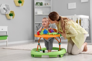 Photo of Mother kissing her little son at home. Cute baby making first steps with toy walker, space for text