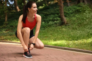 Photo of Smiling woman in sportswear tying shoelaces in park. Space for text