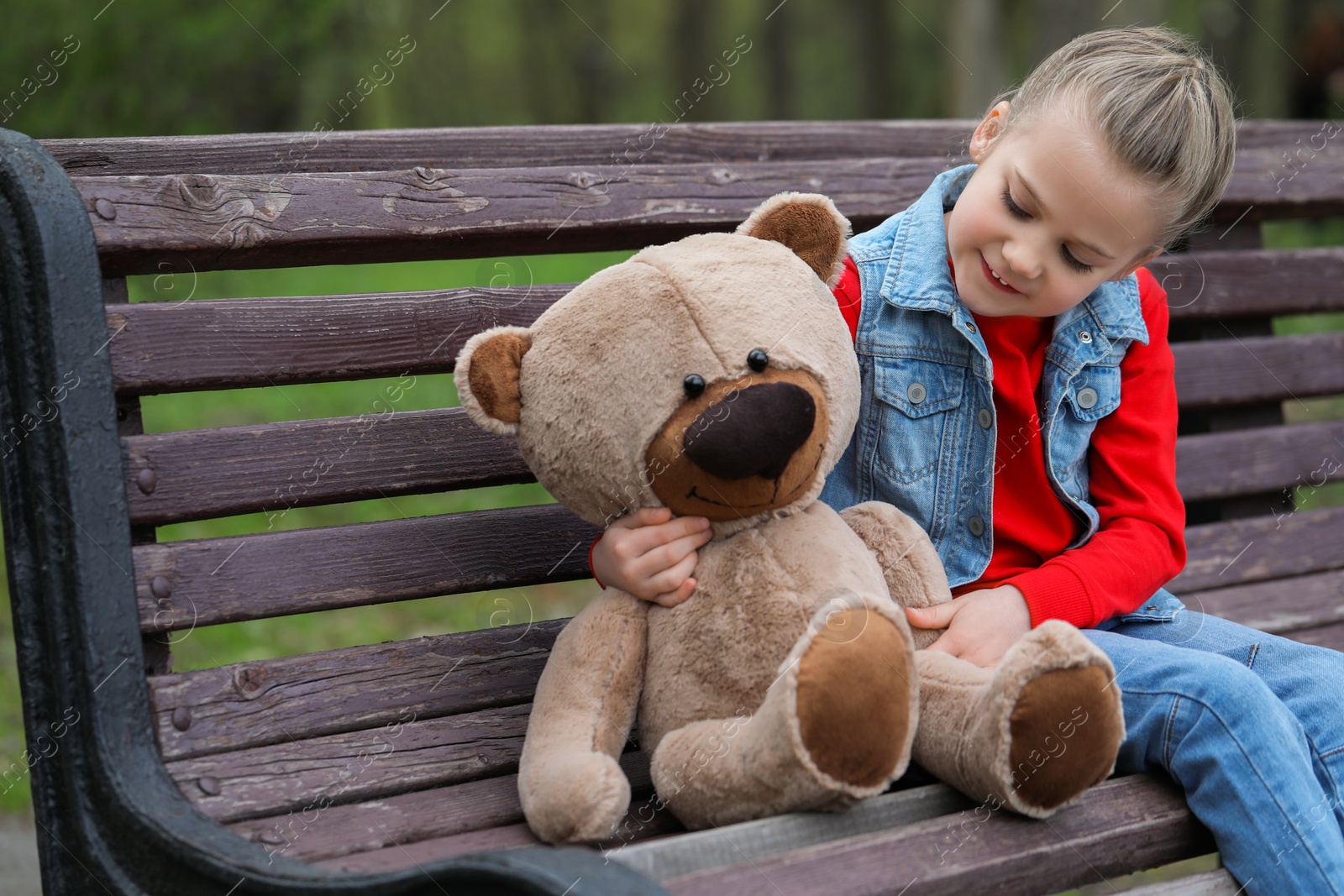 Photo of Little girl with teddy bear on wooden bench outdoors. Space for text