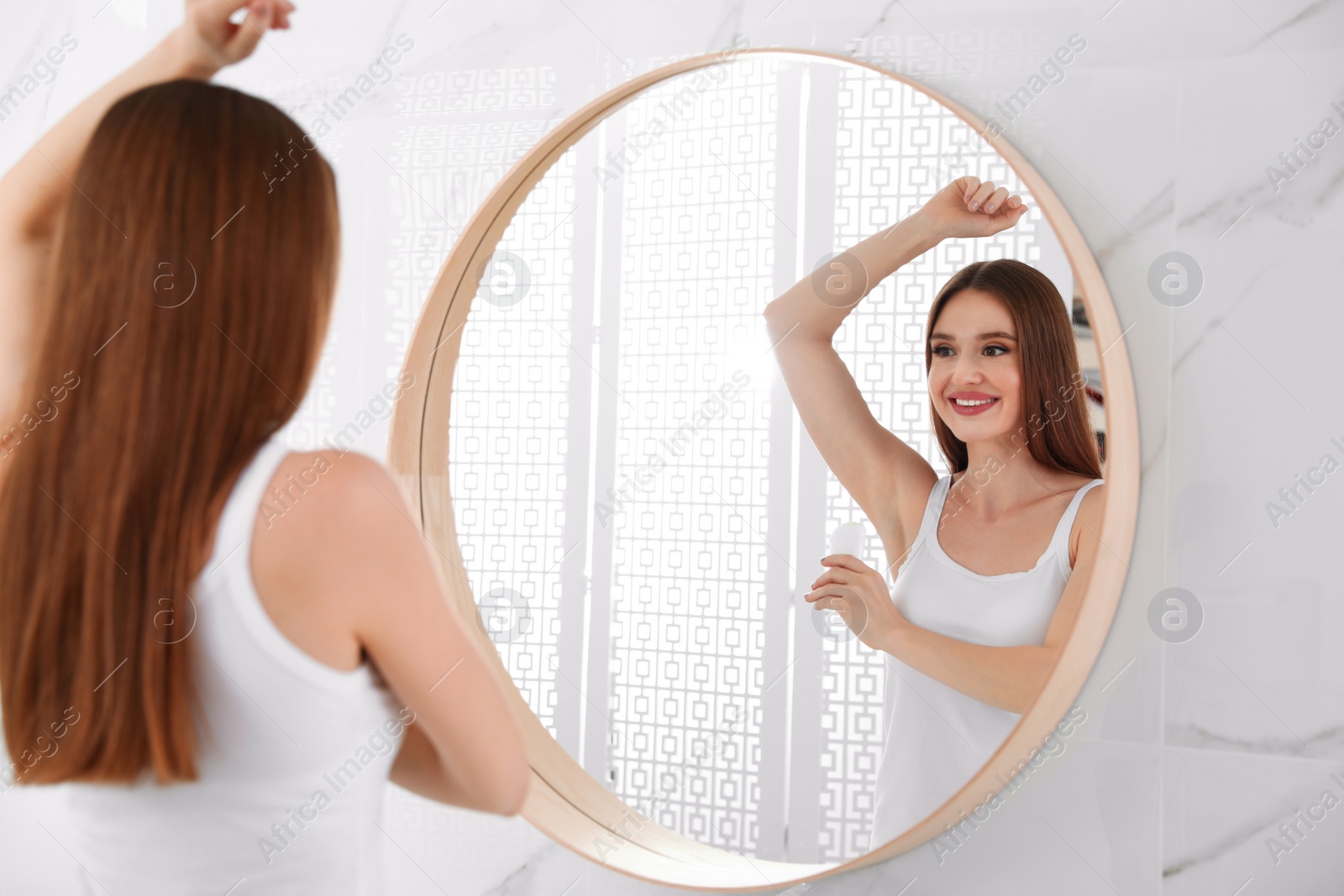 Photo of Beautiful young woman applying deodorant in bathroom